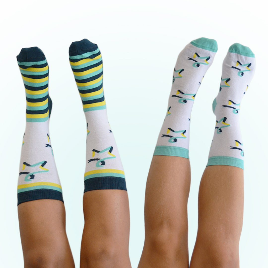 Two pairs of legs are shown from the knees down, with feet pointing upward and wearing our Star of Hope socks. The pair on the left features white socks with the Star of Hope logo and dark teal, yellow, and light teal stripes around the ankles and feet. The pair on the right wears white socks with the Star of Hope logo running vertically down the sides, and light‑teal toes and ankle cuffs.