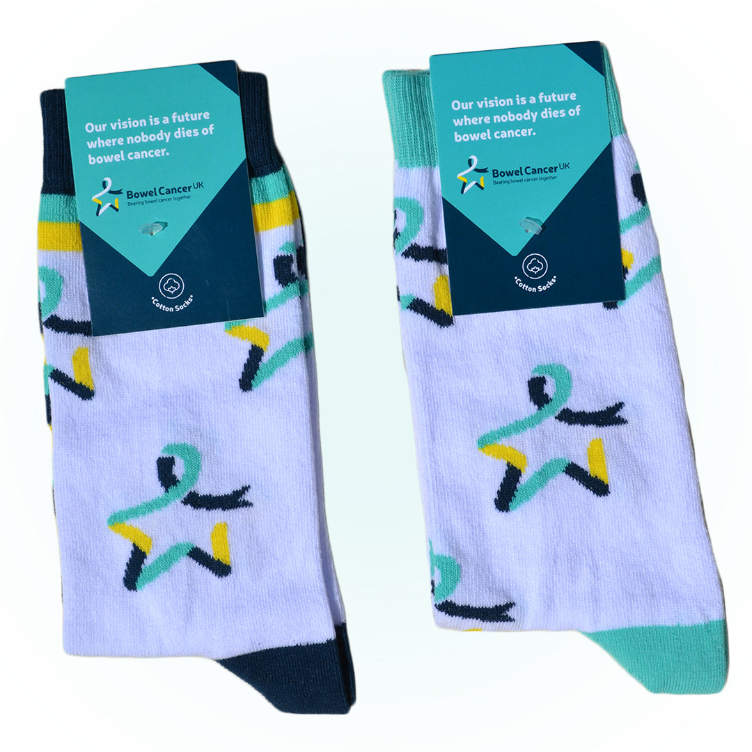Two pairs of our Star of Hope socks are shown with a dark‑ and light‑teal label attached, featuring the text: “Our vision is a future where nobody dies of bowel cancer.” The pair on the left is white with the Star of Hope logo and dark teal, yellow, and light‑teal stripes around the ankles and feet. The pair on the right is white with the Star of Hope logo running vertically down the sides, and light‑teal toes and ankle cuffs.