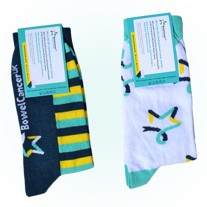 Two pairs of our Star of Hope socks are shown with a dark‑ and light‑teal label attached. The back of the label is visible, displaying the text: “We’re the UK’s leading bowel cancer charity,” along with additional information. The pair on the left is white with the Star of Hope logo and dark teal, yellow, and light‑teal stripes around the ankles and feet. The pair on the right is white with the Star of Hope logo running vertically down the sides, with light‑teal toes and ankle cuffs.