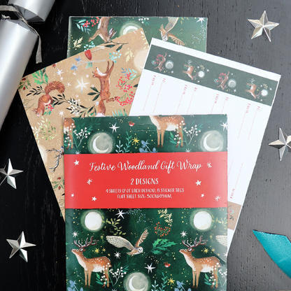 Festive woodland gift wrap set displayed on a dark black wooden surface with silver star decorations and a silver ribbon. The set includes a green wrap with deer, owls, moons and stars, as well as a tan/brown wrap with woodland animals, and a white sheet with printed labels.